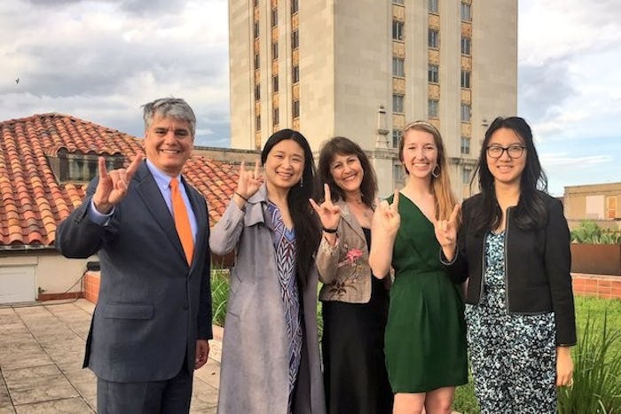 President Greg Fenves, professor Jessie Zhang and students hold up the hook'em symbol in front of the UT Tower