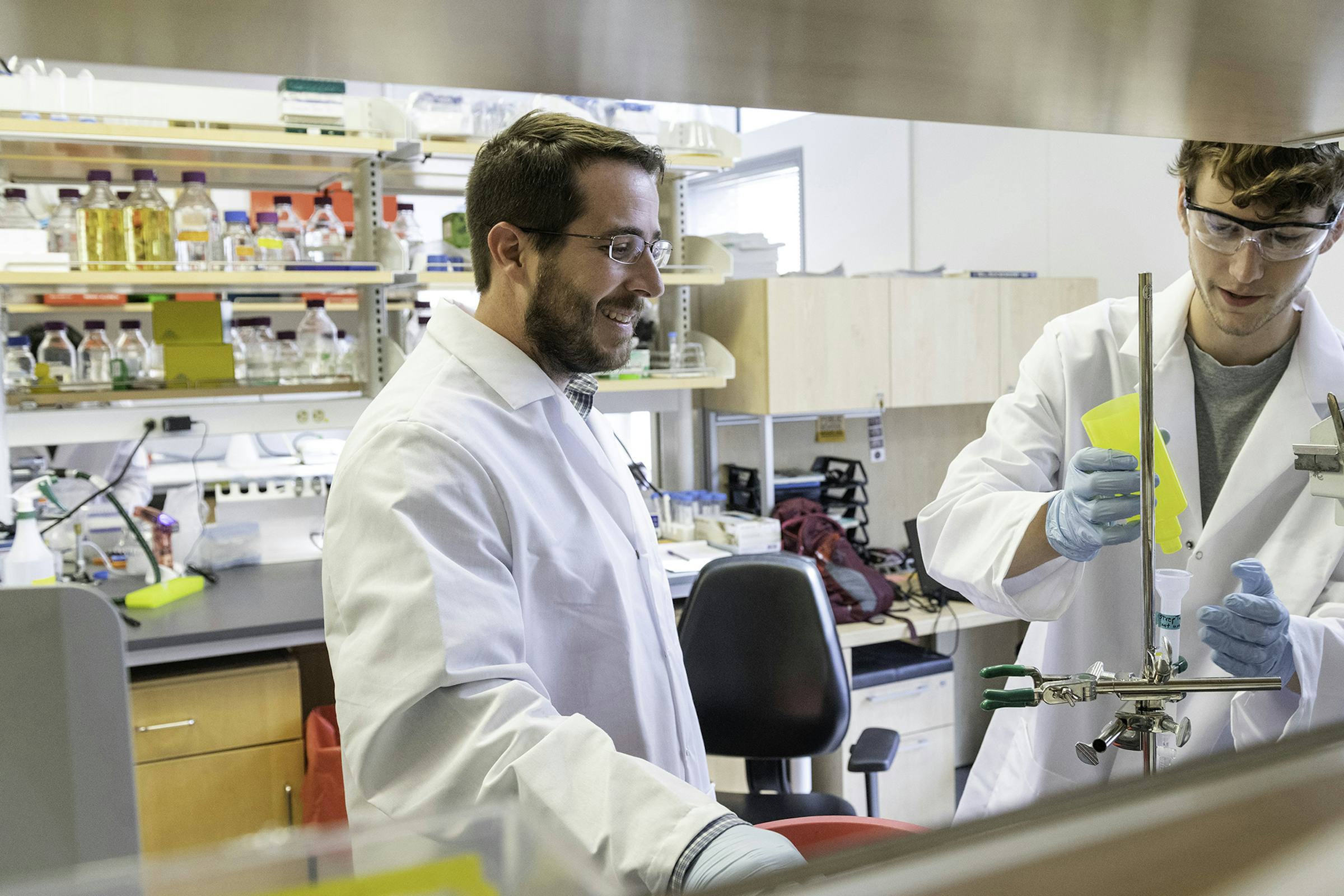 Two scientists in lab coats work at a lab bench.