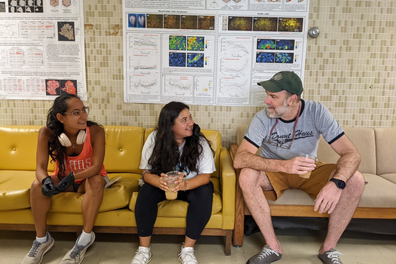 Two undergraduate students sit on a couch next to developmental biologist John Wallingford